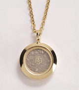 Gold necklace with a round pendant on a light gray background